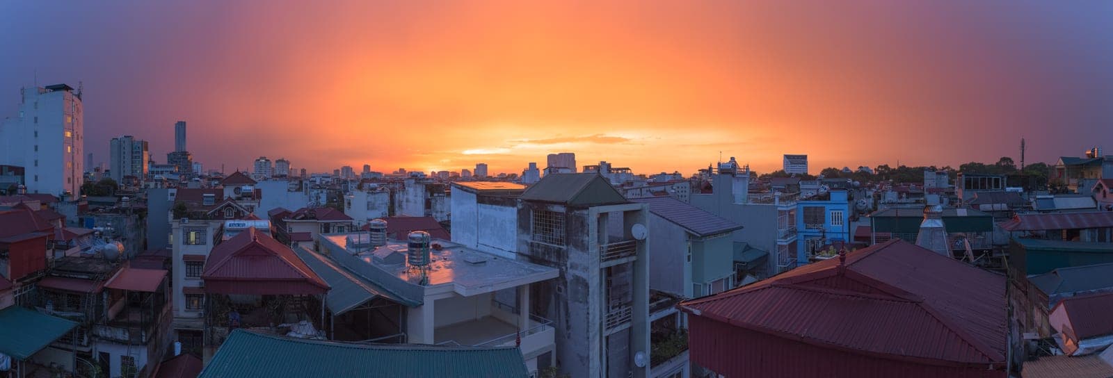 Golden sunset light reflecting off wet streets and rooftops of Hanoi after rain, with the city glowing warmly beneath clouds.
