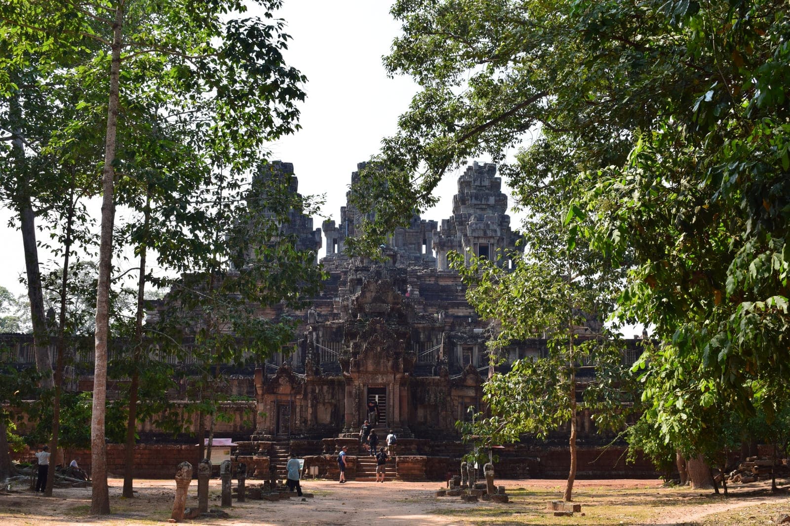 A traditional wooden Buddhist temple with multi-tiered architecture and ornate details, photographed during daylight with surrounding tropical vegetation
