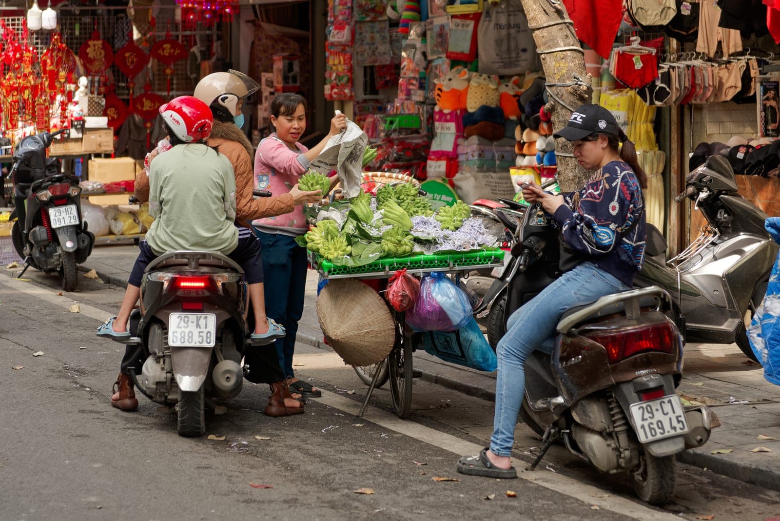 Street vendor with baskets of fingered citrons in Hanoi's Old Quarter, surrounded by traditional shophouses and urban market atmosphere.