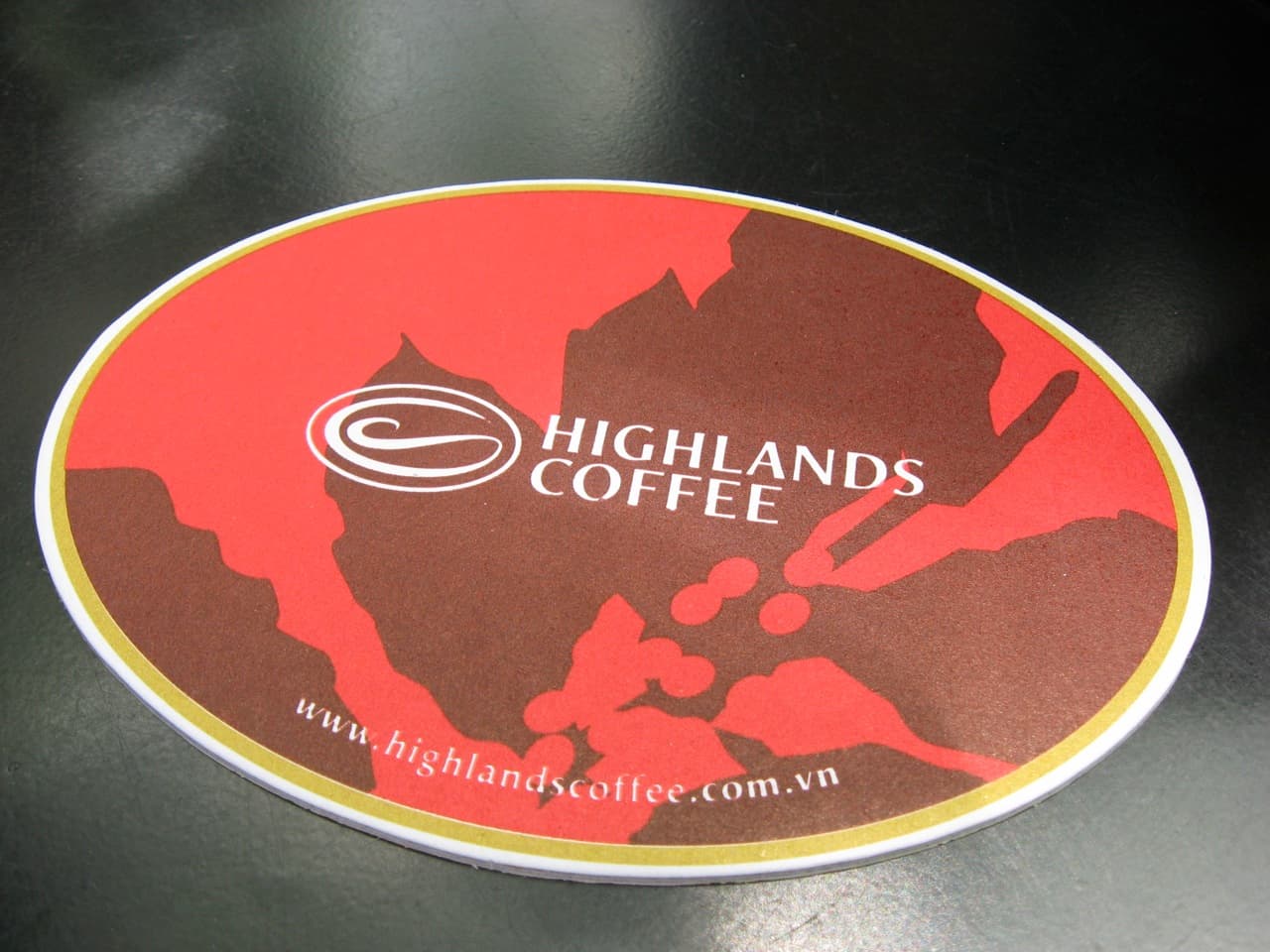 A white Highlands Coffee branded coaster displayed on a neutral background