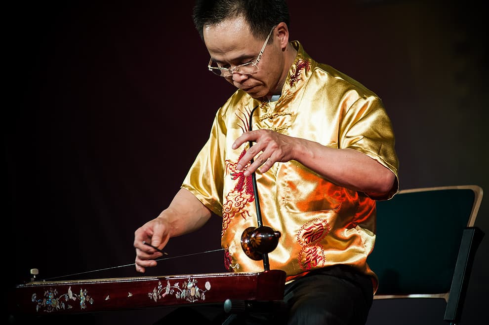 Close-up view of a wooden dan bau one-string monochord with a flexible rod, displaying the Vietnamese instrument's distinctive curved soundbox and string arrangement.