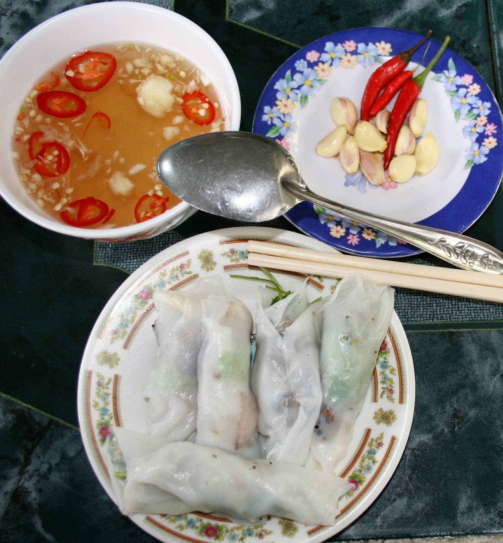 Translucent steamed rice pancakes rolled with minced pork filling, served on a plate with fresh herbs and dipping sauce