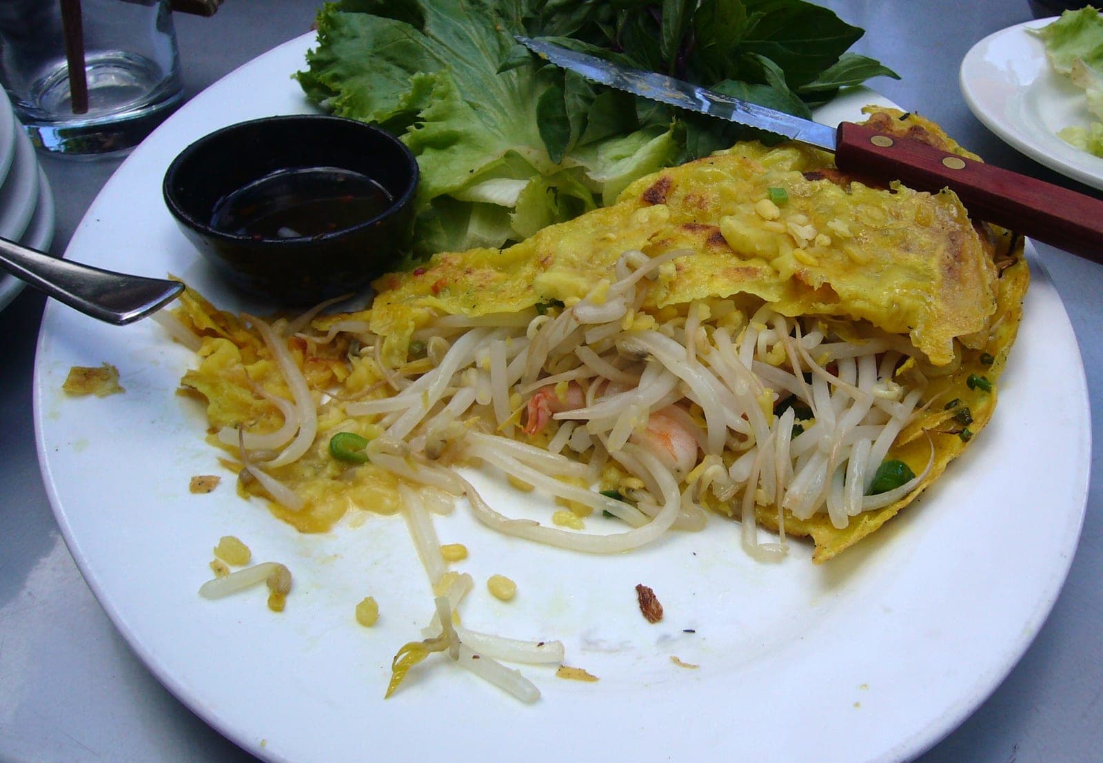 Golden sizzling bánh xèo crepe folded on a plate, served with fresh herbs and lettuce for wrapping