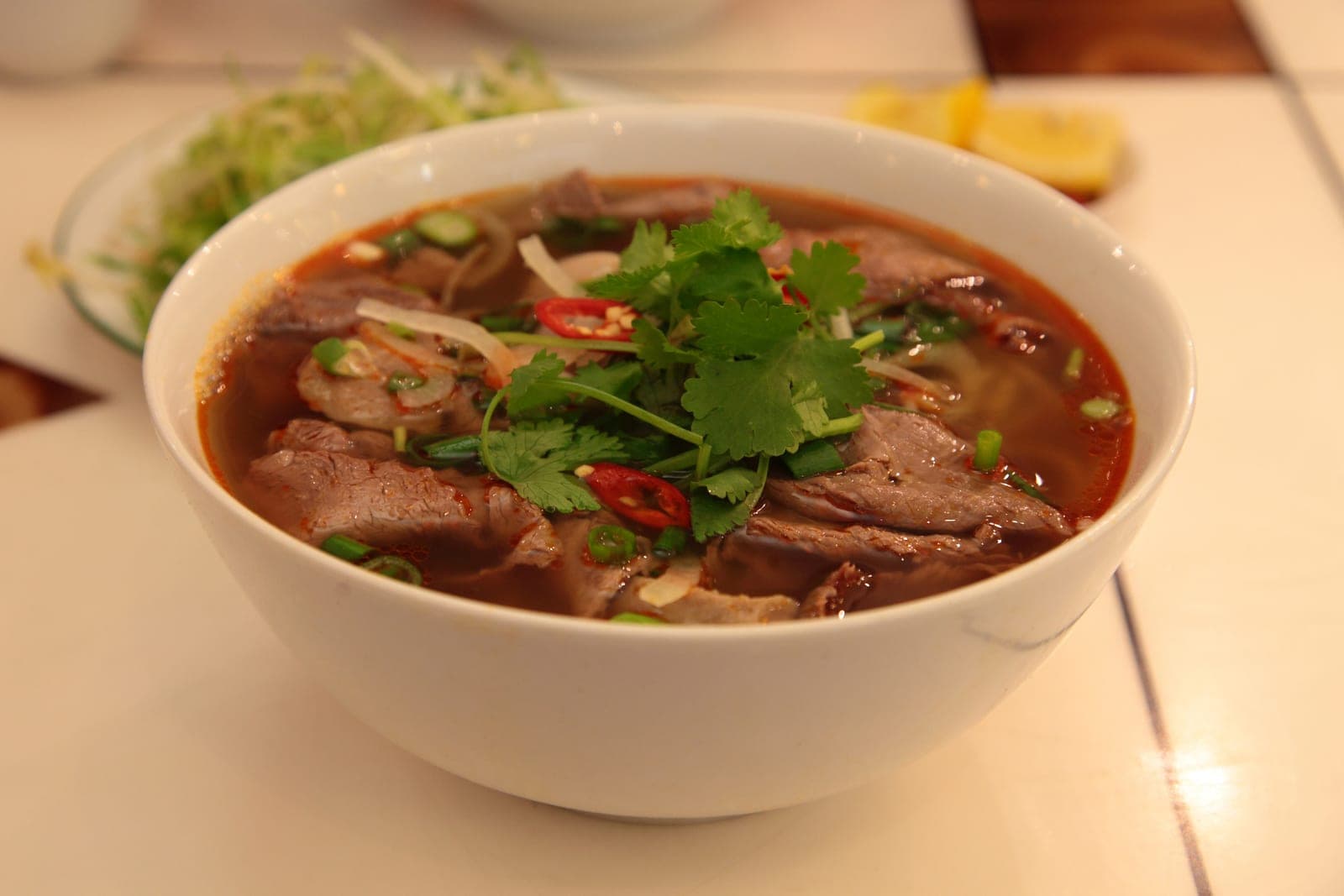Deep red beef and pork noodle soup in a white bowl with fresh herb garnish