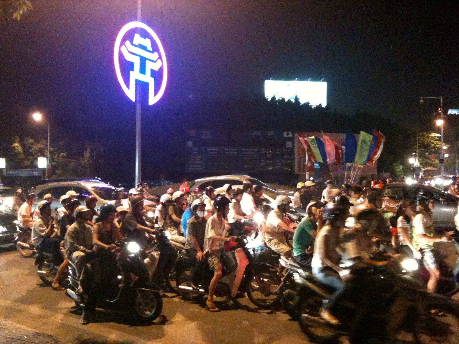 Busy Hanoi street with motorbikes, scooters, and cyclists flowing through a congested urban intersection during daytime traffic