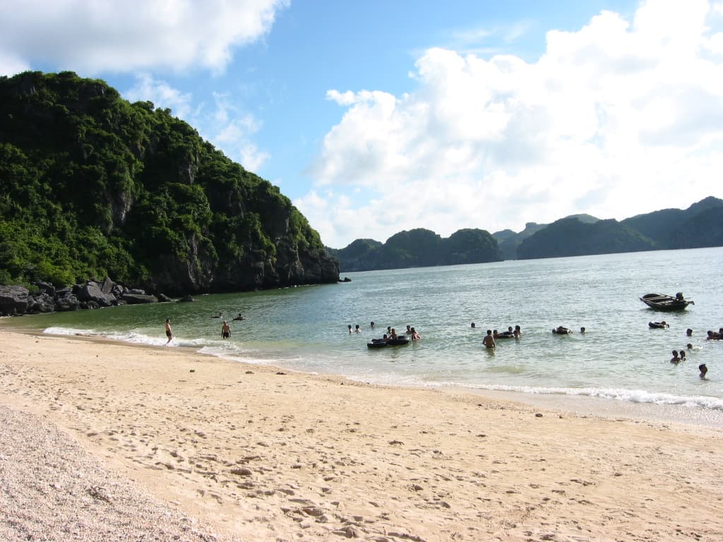 Sandy beach with calm turquoise water surrounded by dramatic limestone karst mountains in Cat Ba island