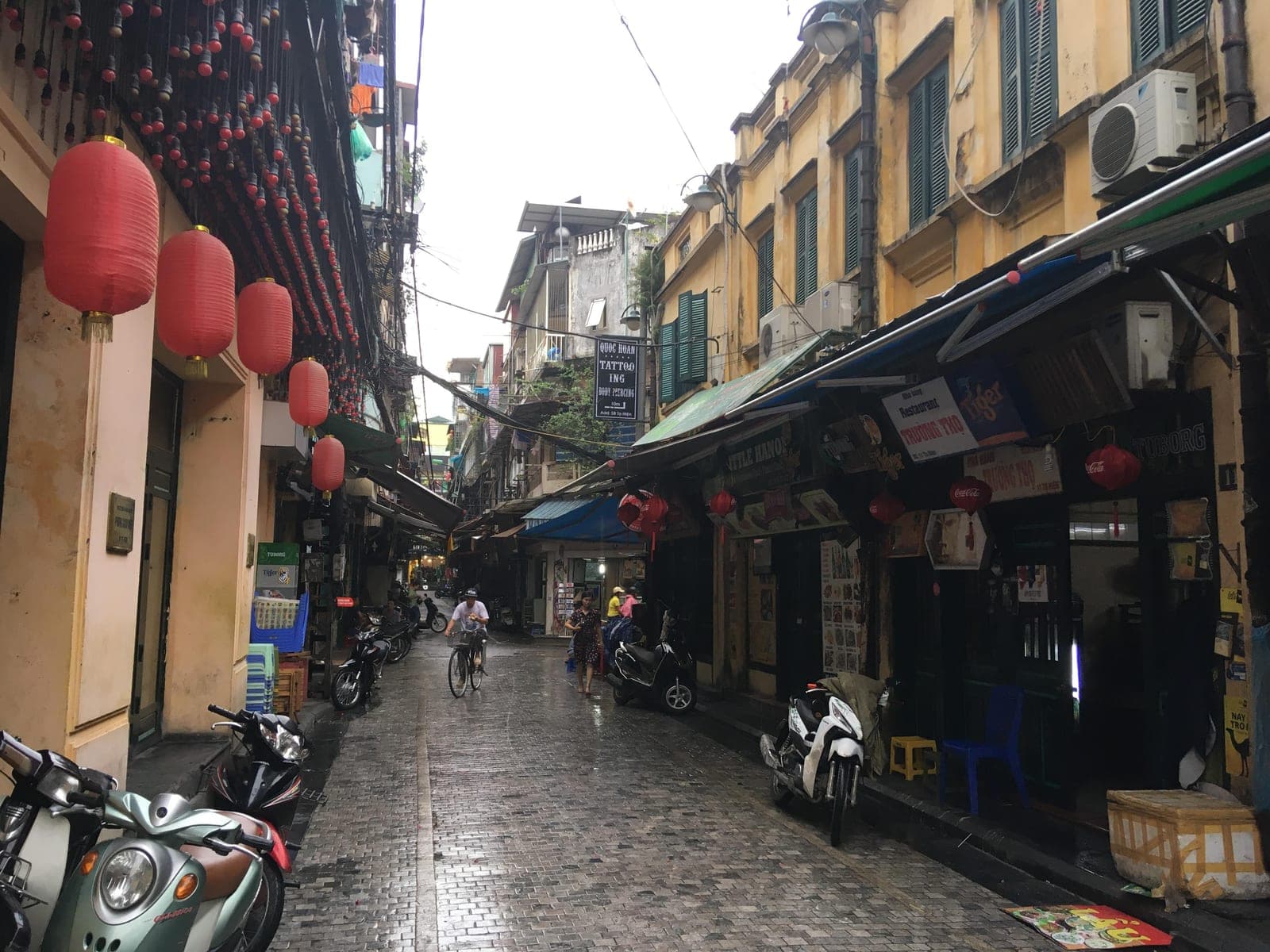 Tạ Hiện Street in Hanoi's Old Quarter with traditional colonial-era buildings, shop signs, and narrow cobblestone street lined with storefronts