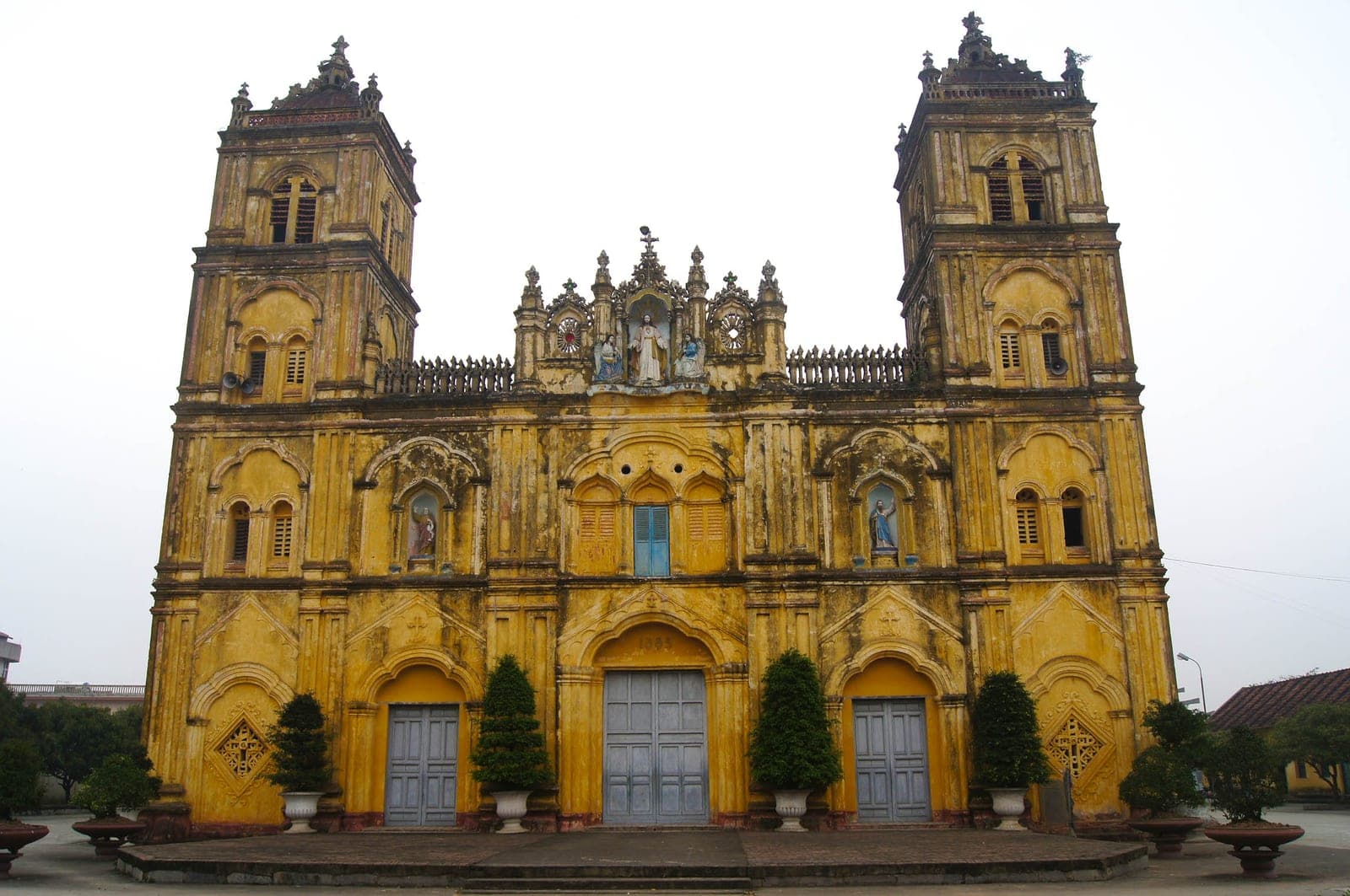Stone facade of Bùi Chu Cathedral in Nam Định, showcasing French Gothic architecture with Vietnamese decorative elements and traditional ornamentation.